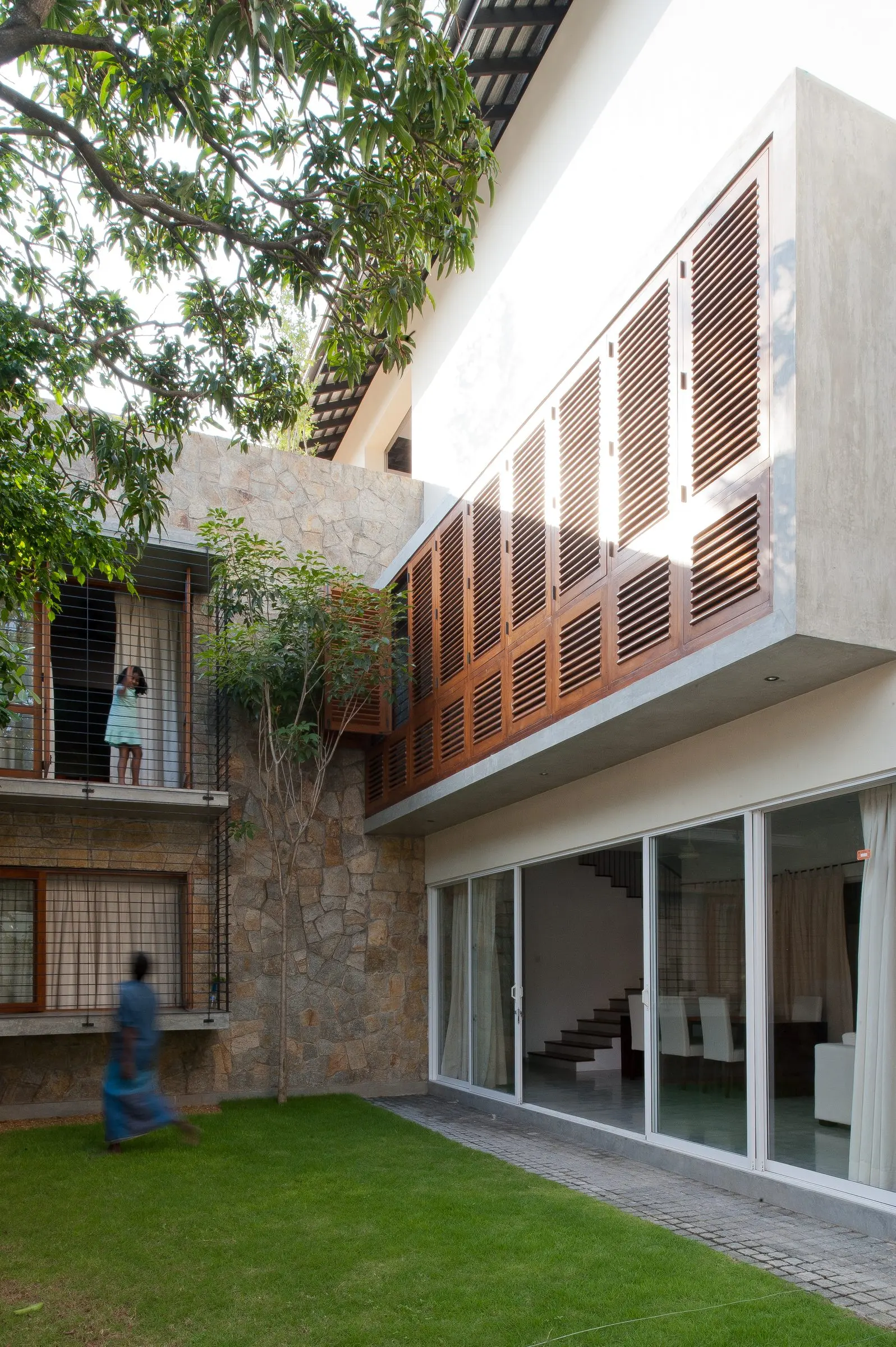 The courtyard by day: the timber-louvred upper floor above glazed doors, with a tree and a lawn.