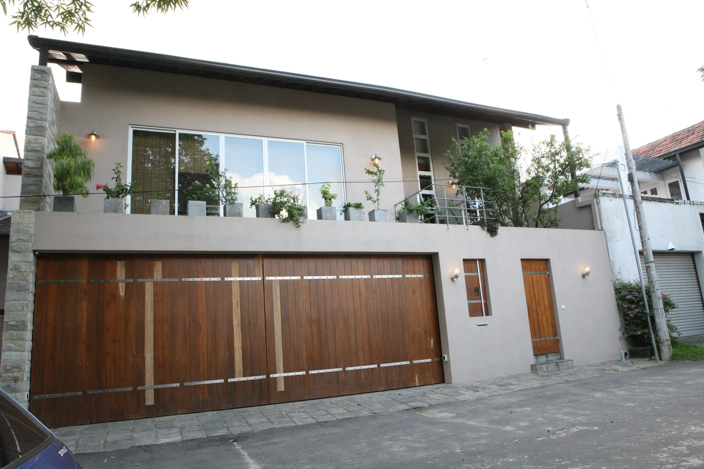 The street elevation: a two-storey house with a large garage gate, a planted upper terrace and a glazed upper floor.