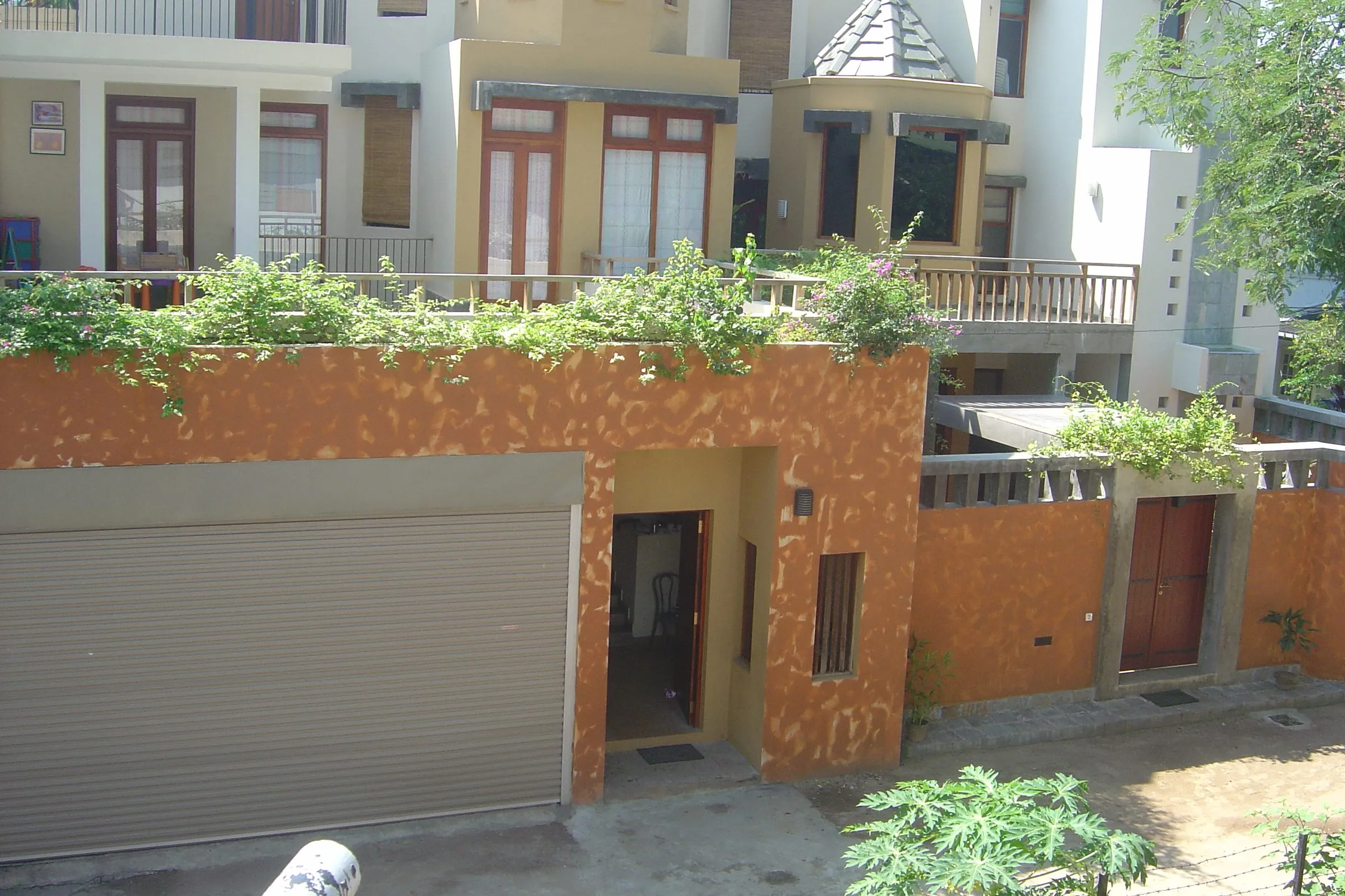 The street front: an orange wall and a garage door below a planted terrace, with the turreted upper floors behind.