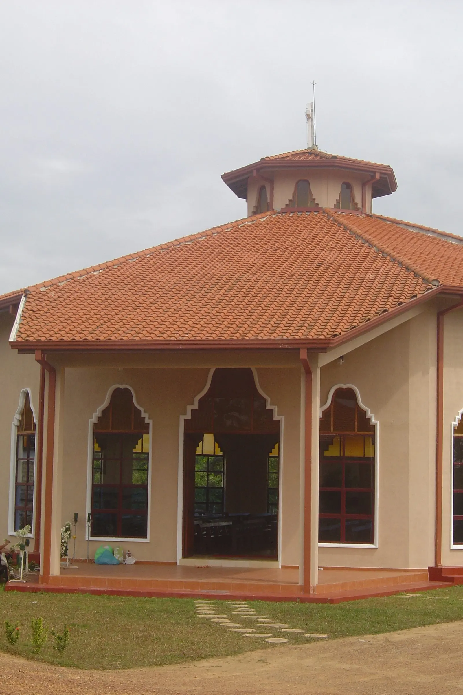 A corner of the church: a tiled roof over a covered porch, and arched windows with red frames.