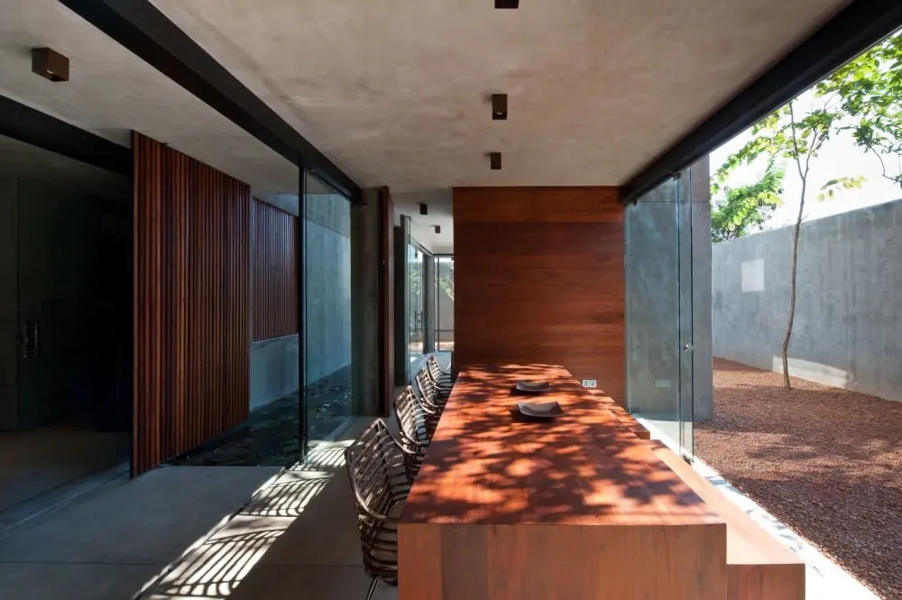 A long dining table in a glazed gallery beside a walled garden.