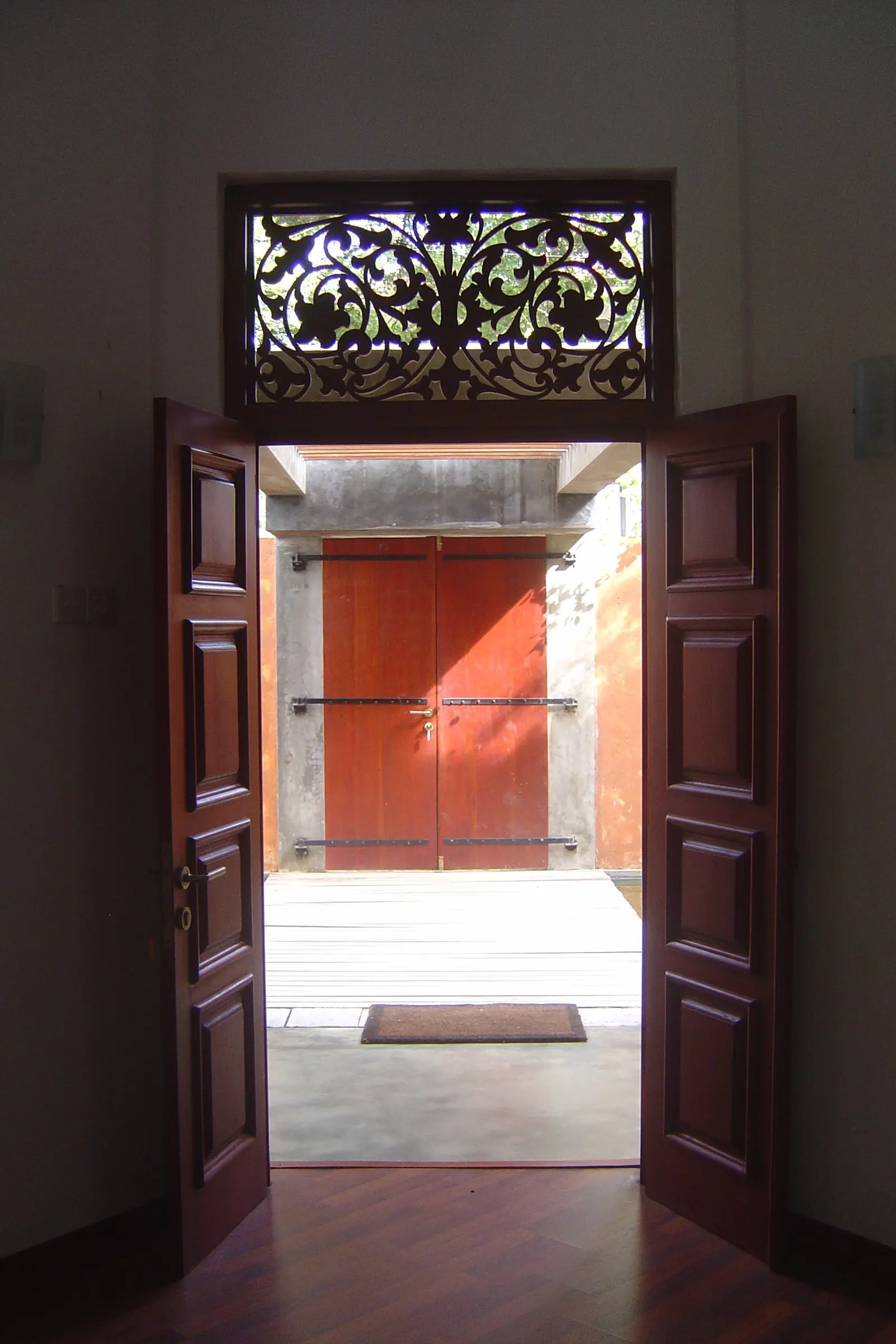Double doors with a carved fanlight, opening onto a hallway with a red door beyond.