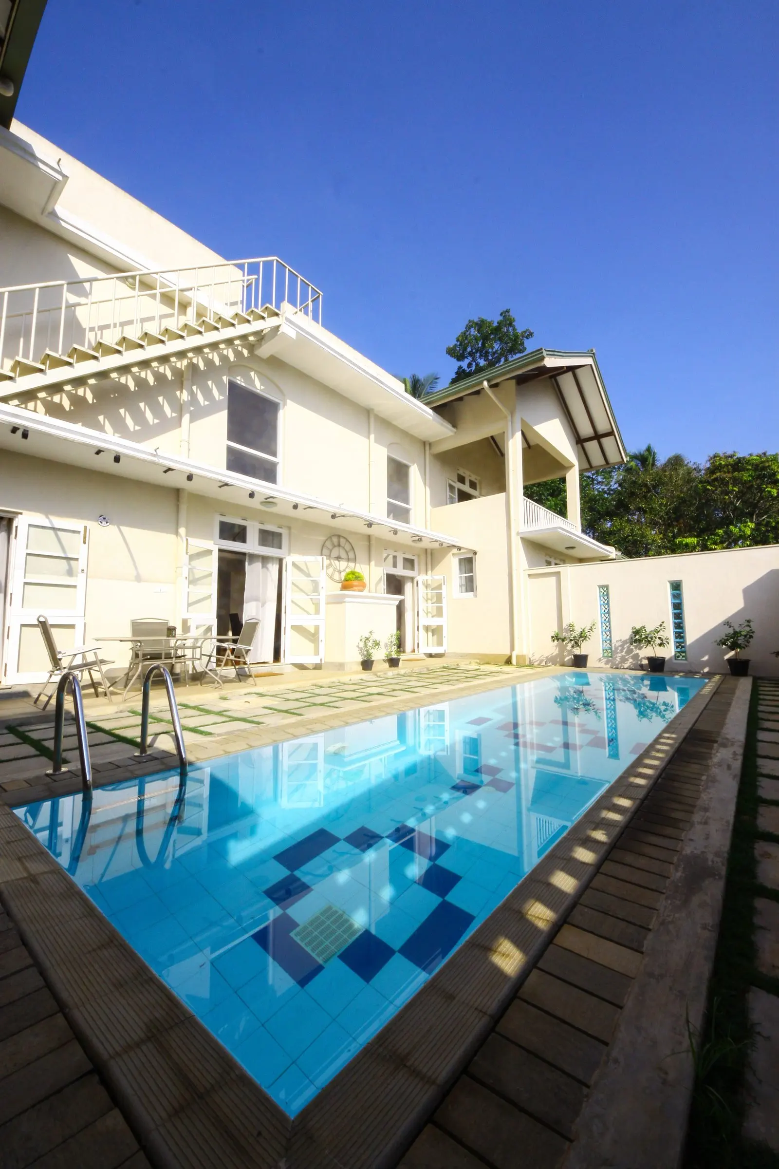A swimming pool beside a white two-storey house.