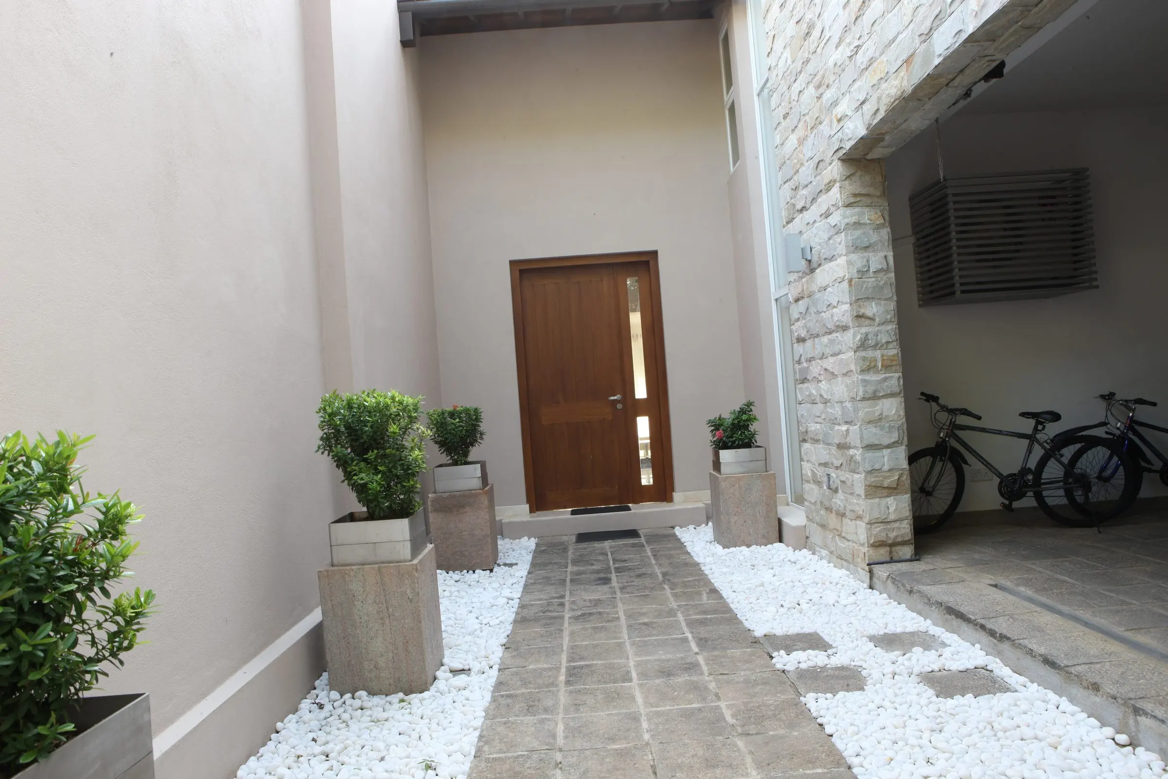 A narrow entrance court with a door, planters and white pebbles.