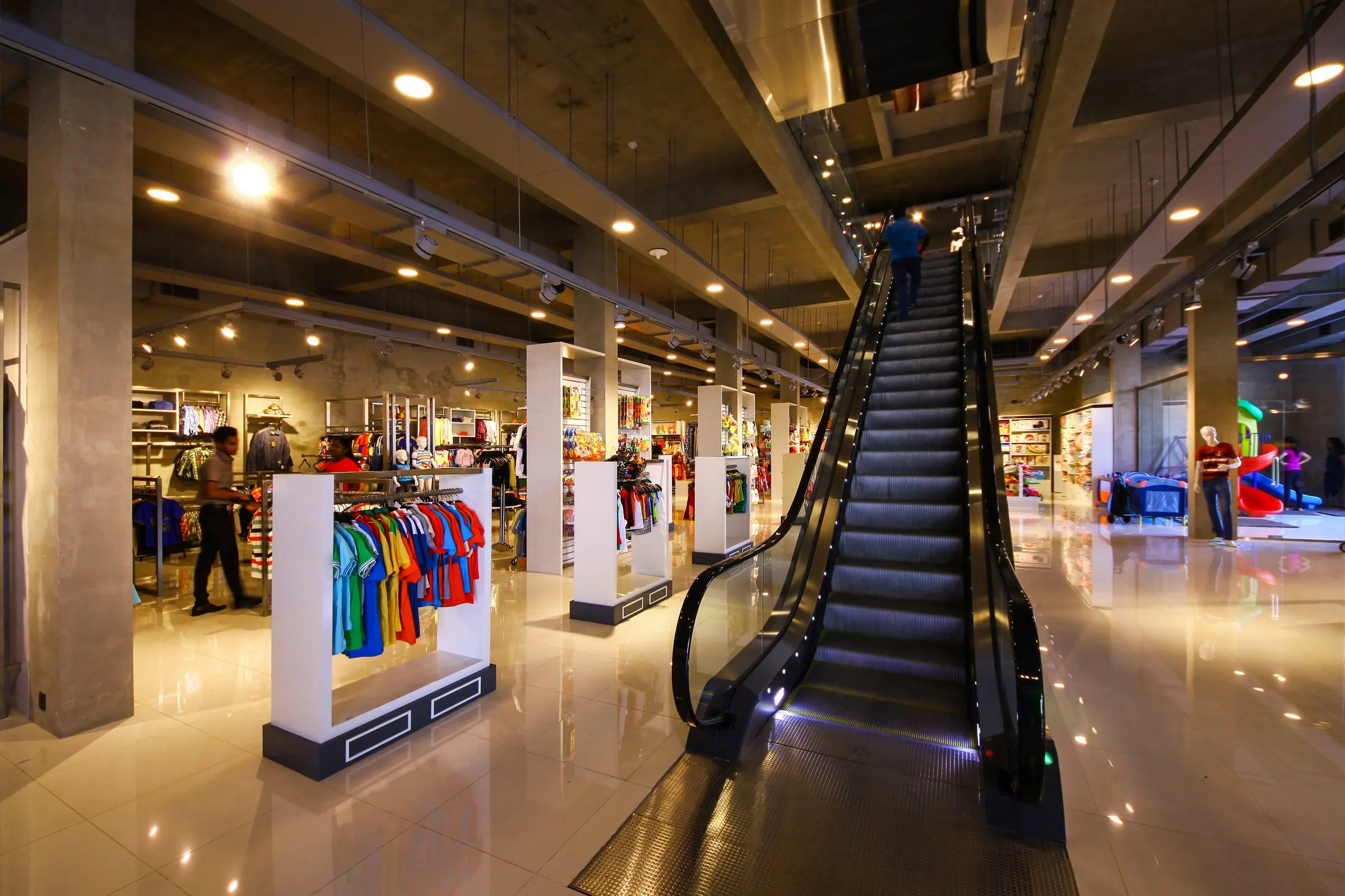 A retail floor with an escalator and track lighting.