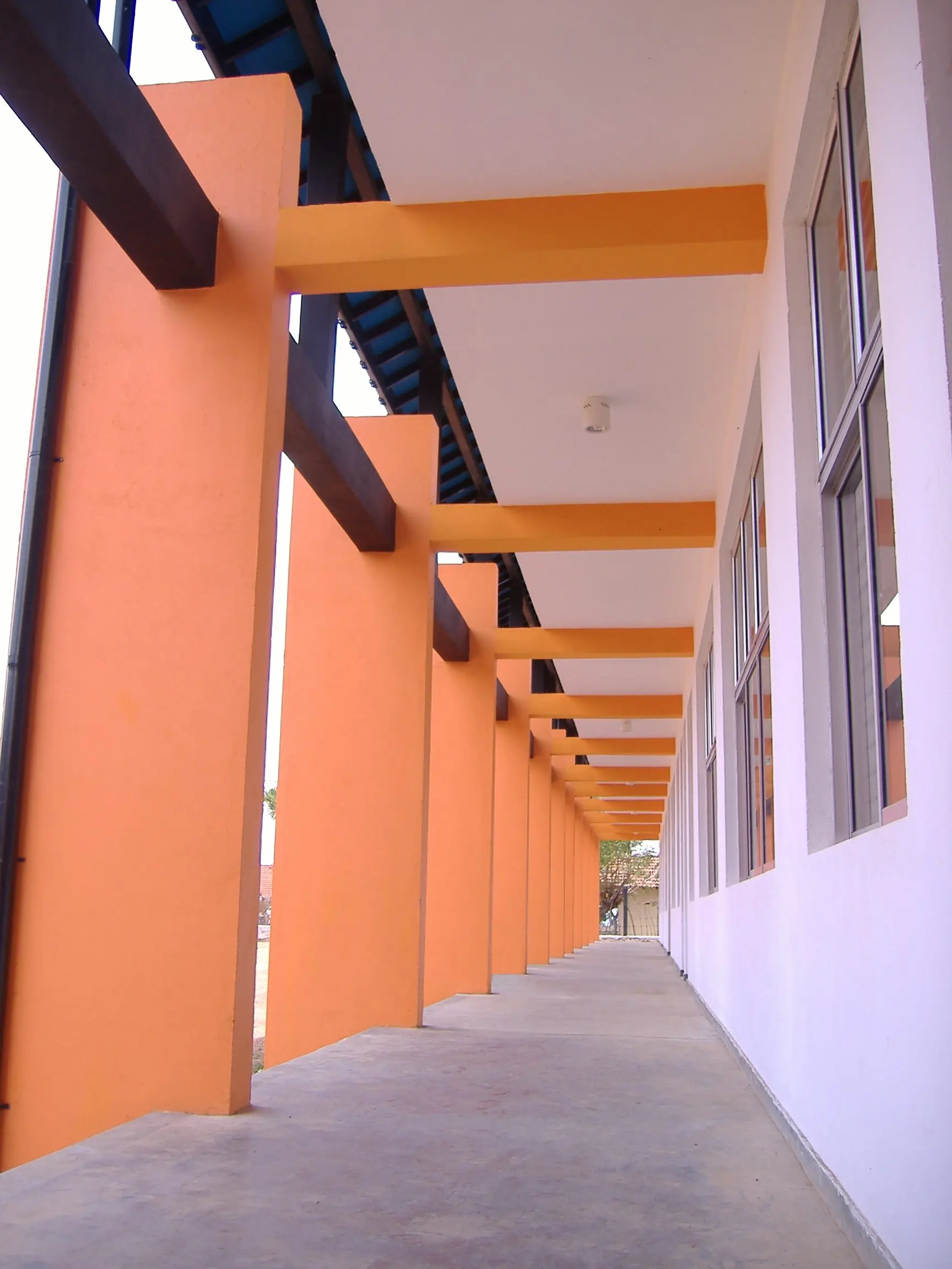 A covered walkway with orange columns and beams along a white wall.