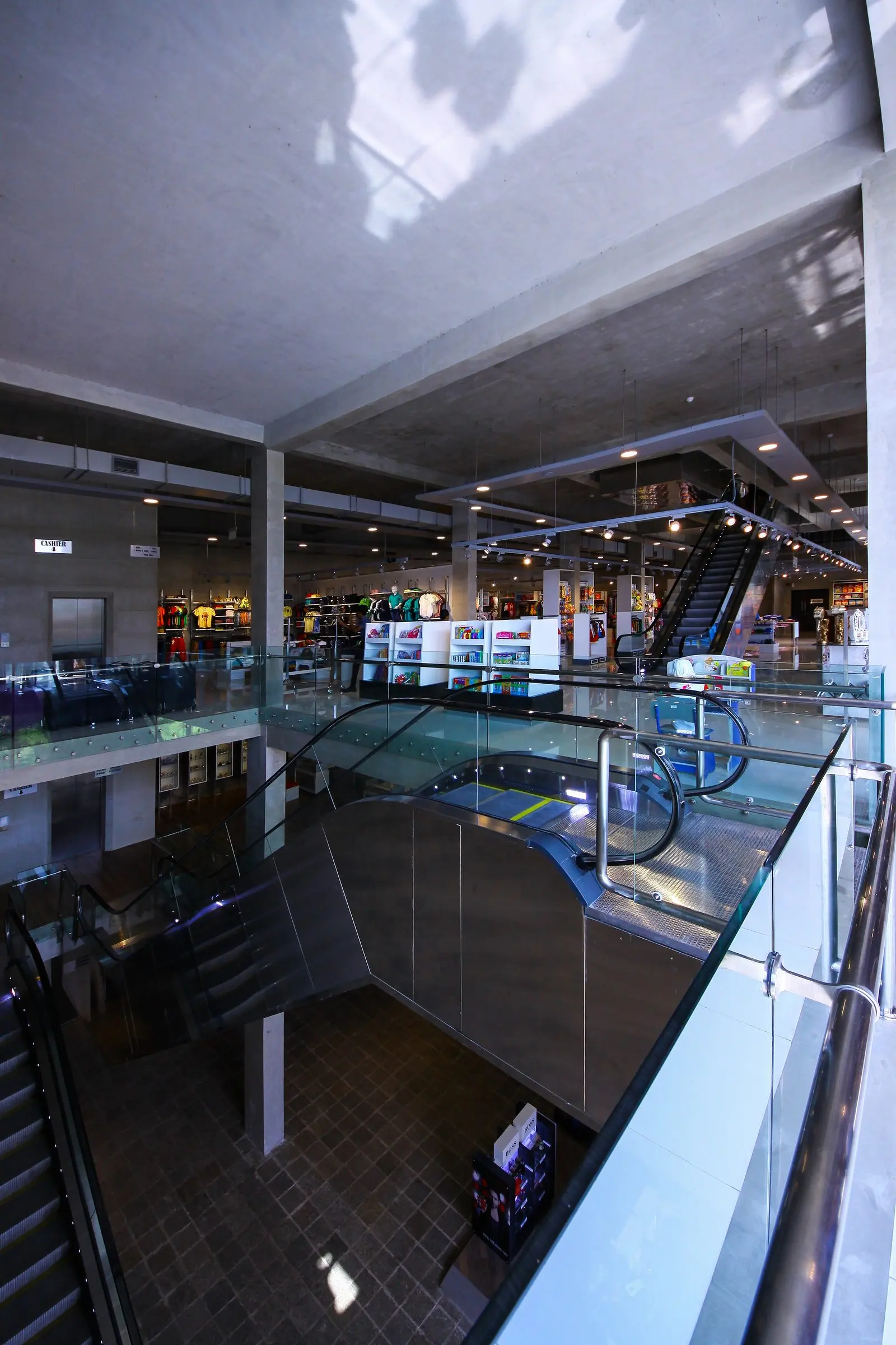 A multi-storey interior seen from an upper floor, with glass balustrades, escalators and a skylight.