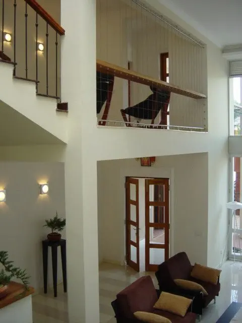 A double-height living space with a stair balustrade, wall lights and a pair of armchairs.