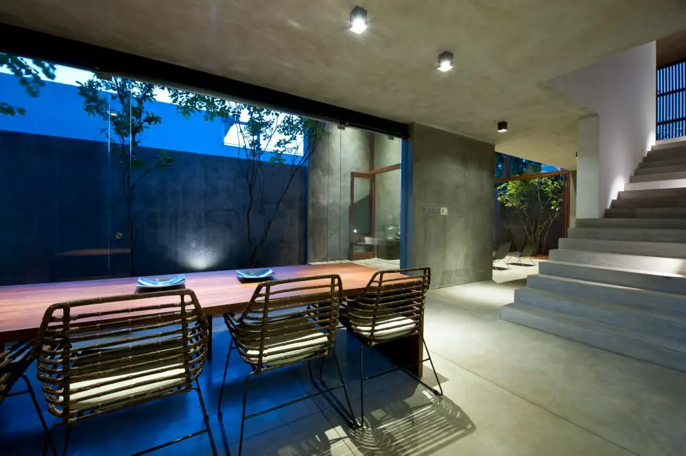 The dining area at night, with a stair beside glazed walls and a lit garden beyond.