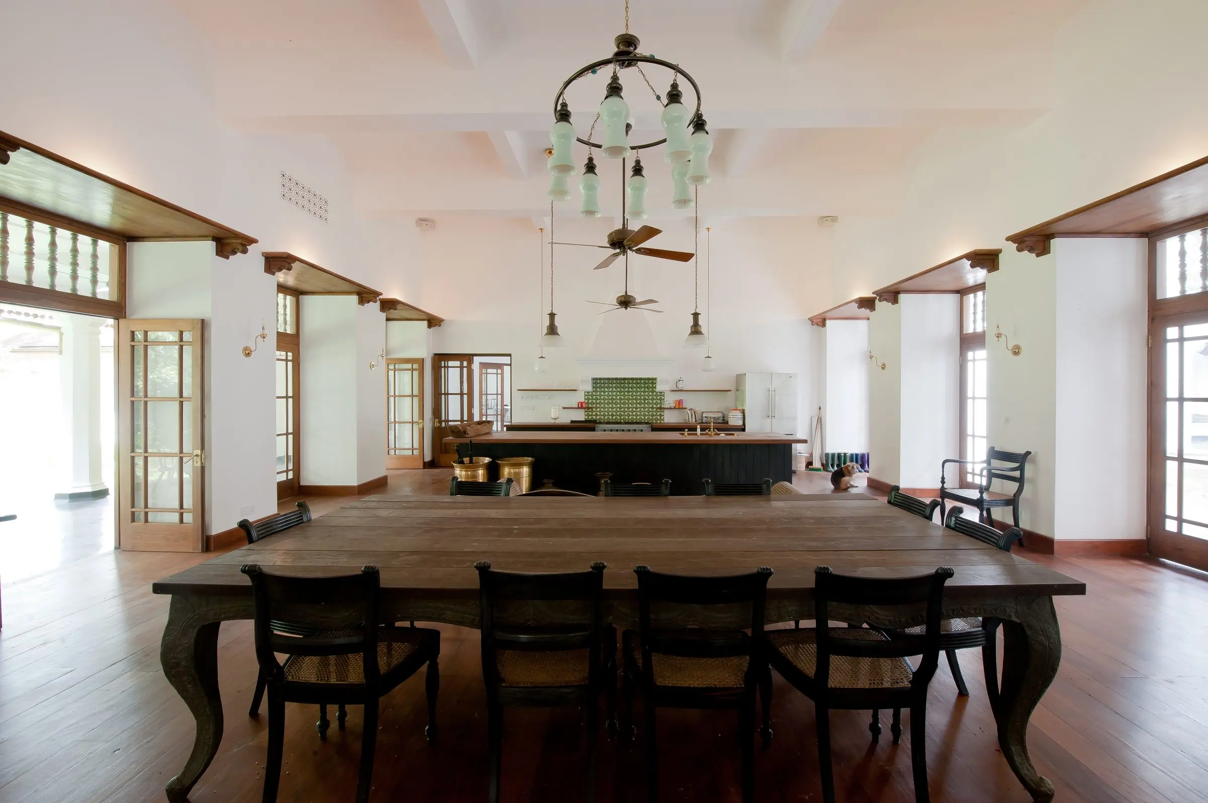 A long dining table in a white double-height hall with a chandelier.