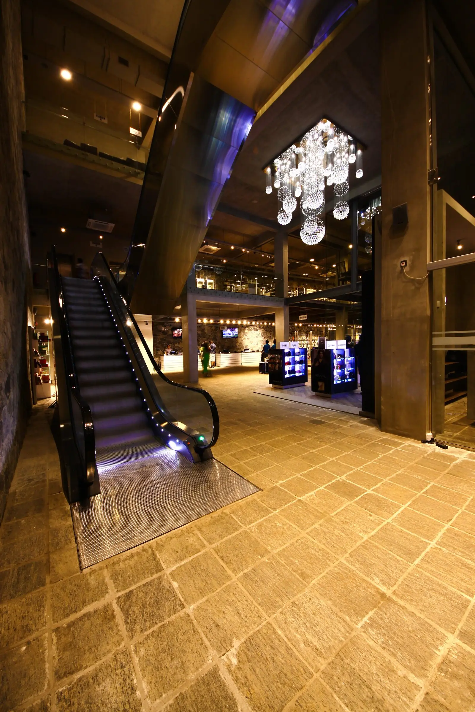 A ground-floor lobby with stone paving, a lit escalator and a chandelier — Commercial Building, Rajagiriya.