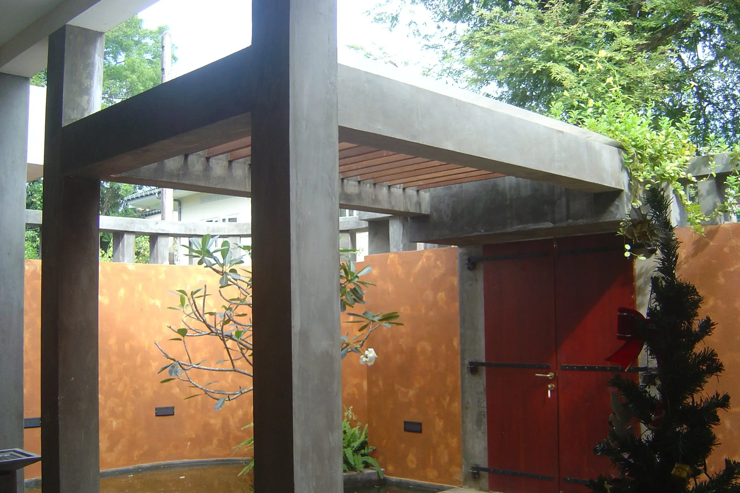A pergola over a courtyard, with a red door and an orange wall — House at Wijayarama Mawatha, Colombo 07.