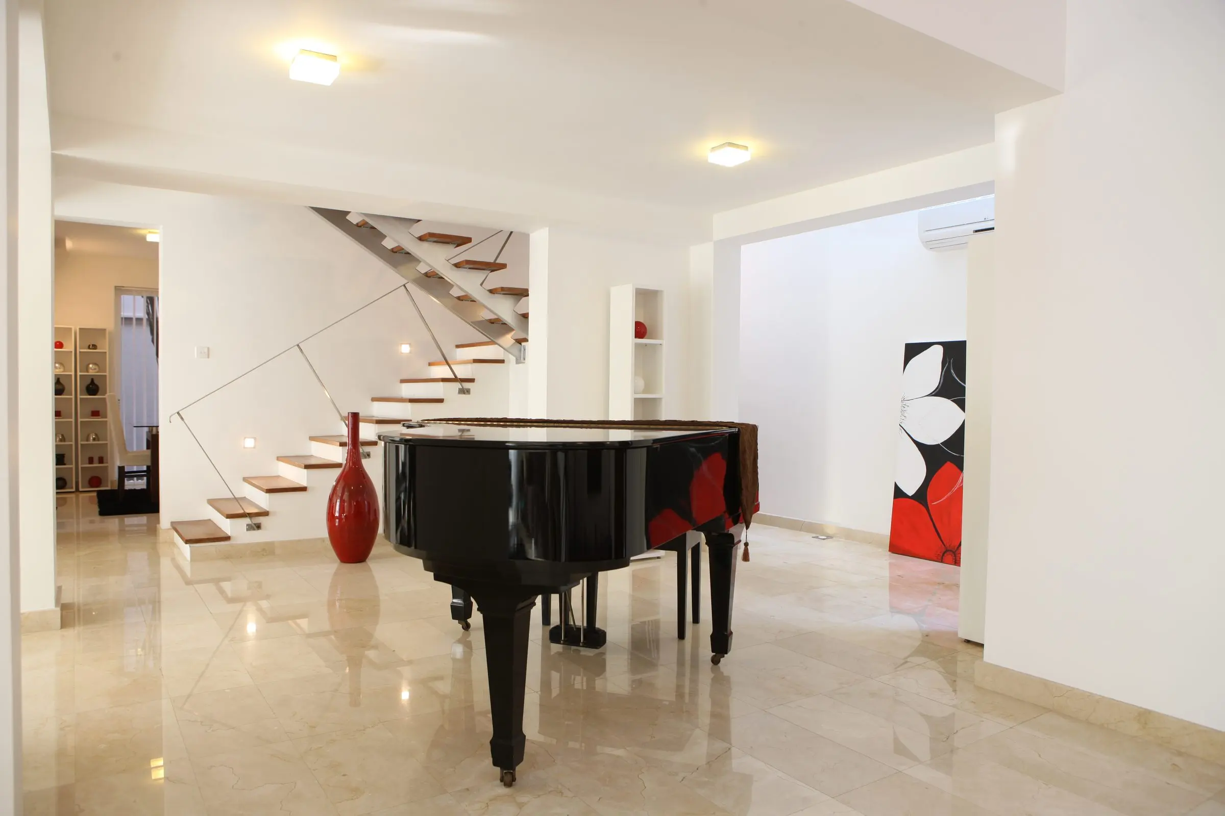 A stair hall with a floating stair, a grand piano and red artwork.