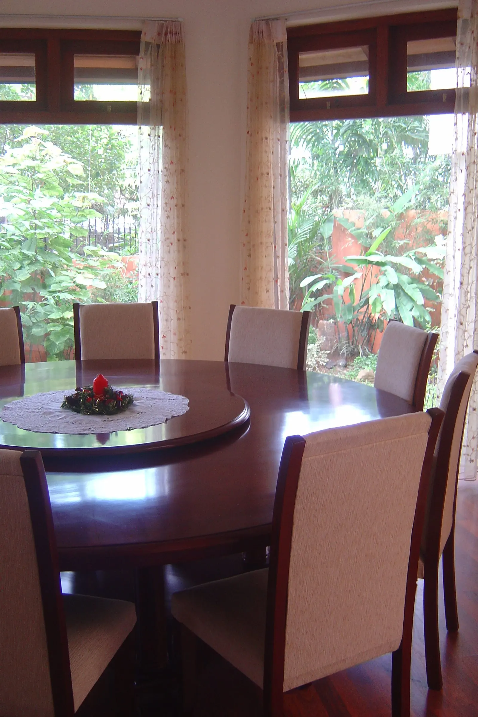 A round dining table and upholstered chairs beside tall windows and curtains.