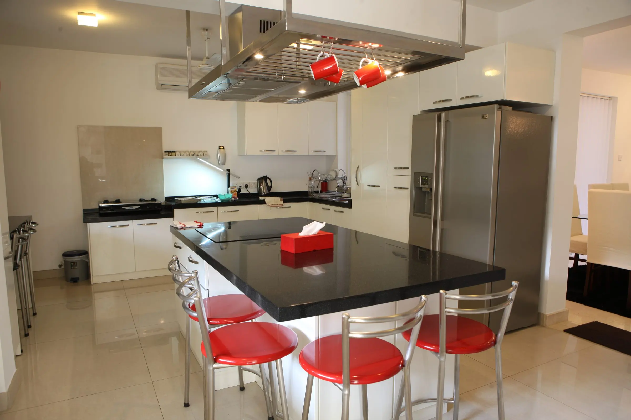 A kitchen with a black island counter, red bar stools and a cooker hood.