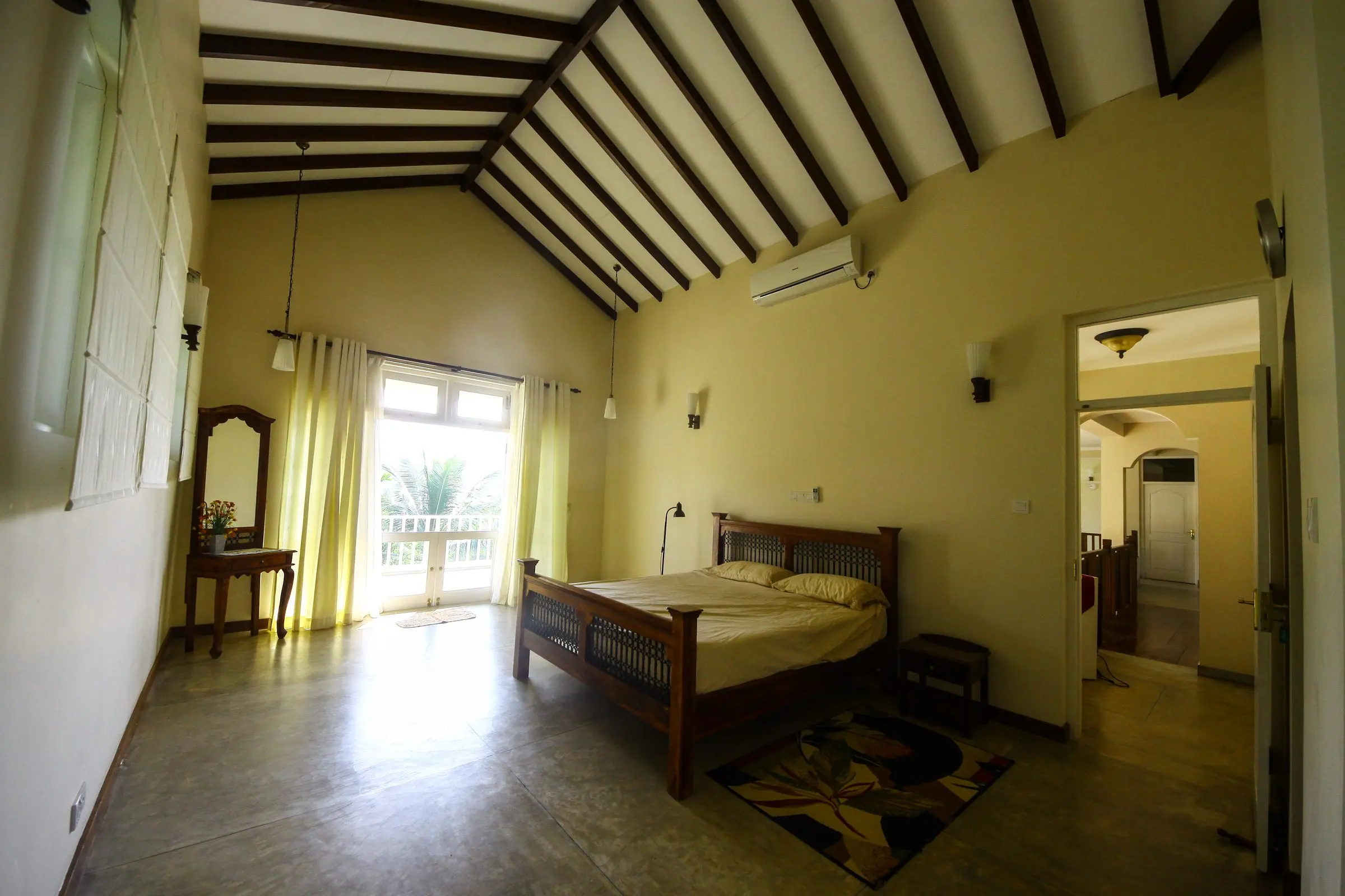 A bedroom under a pitched ceiling, with a four-poster bed and a balcony door.