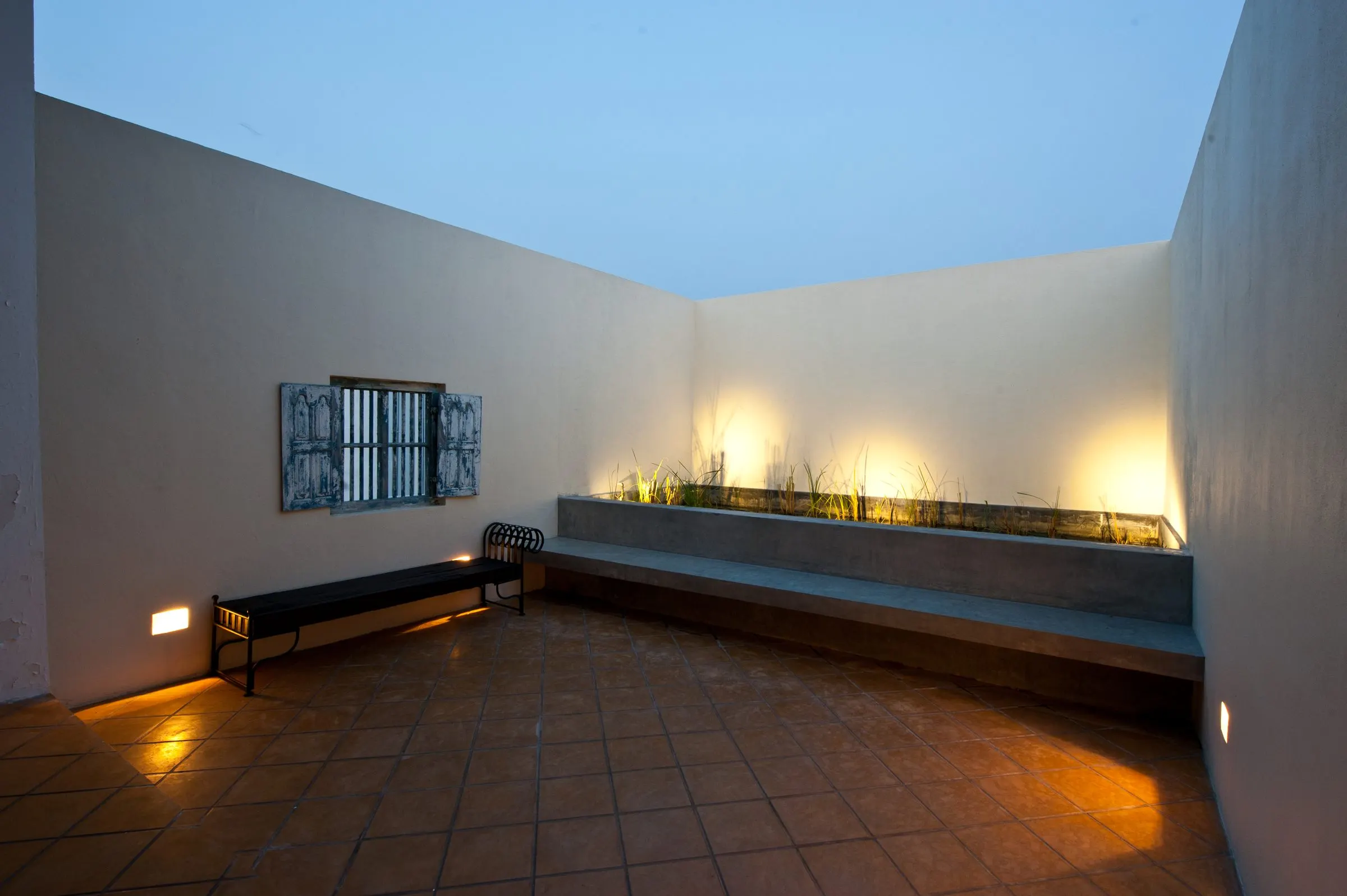 The terrace at dusk, with terracotta tiles, planting and lighting along a ledge.