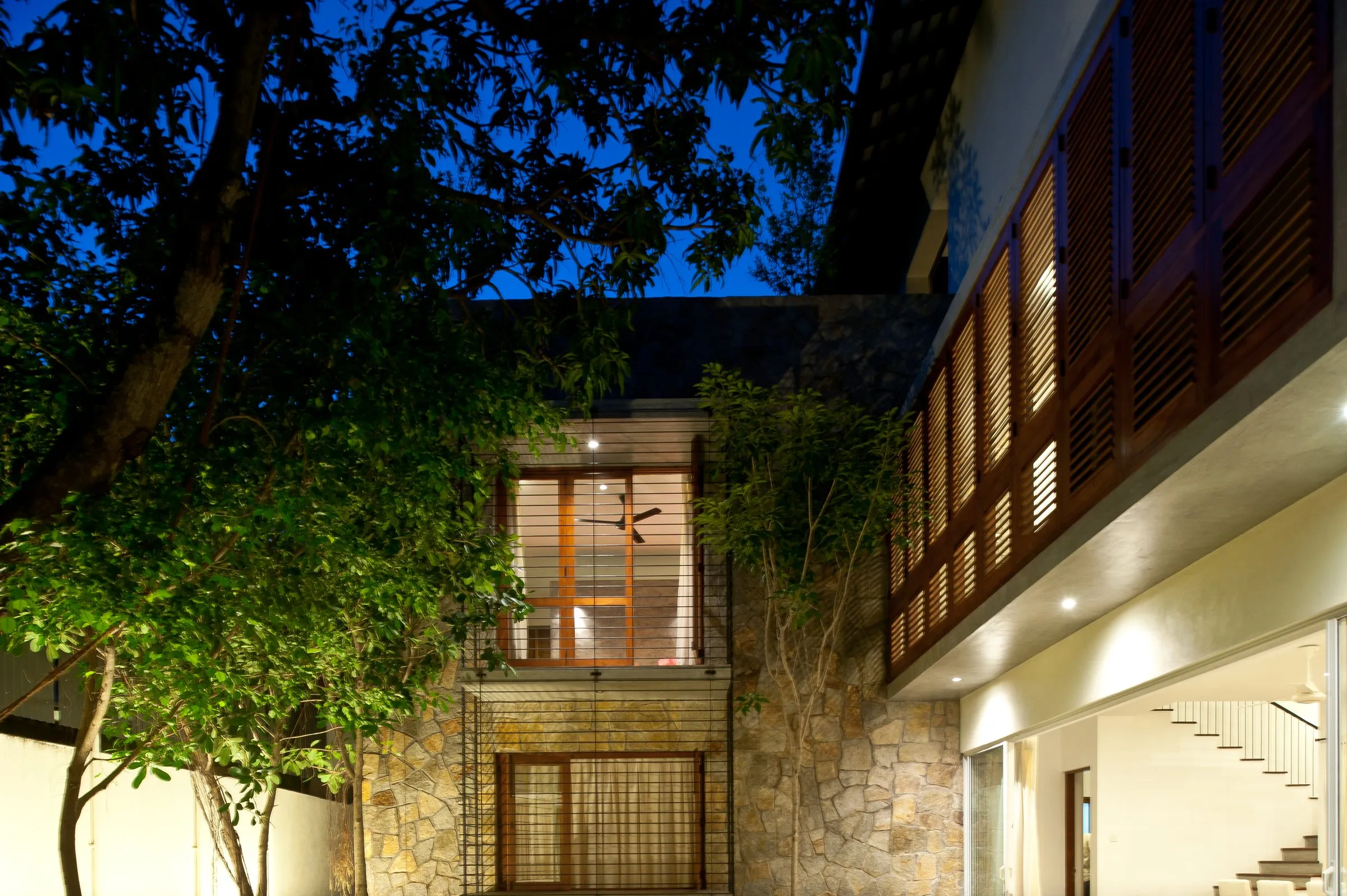 The courtyard at night, with a tree, a lit stone clad wall and the timber-louvred upper floor.