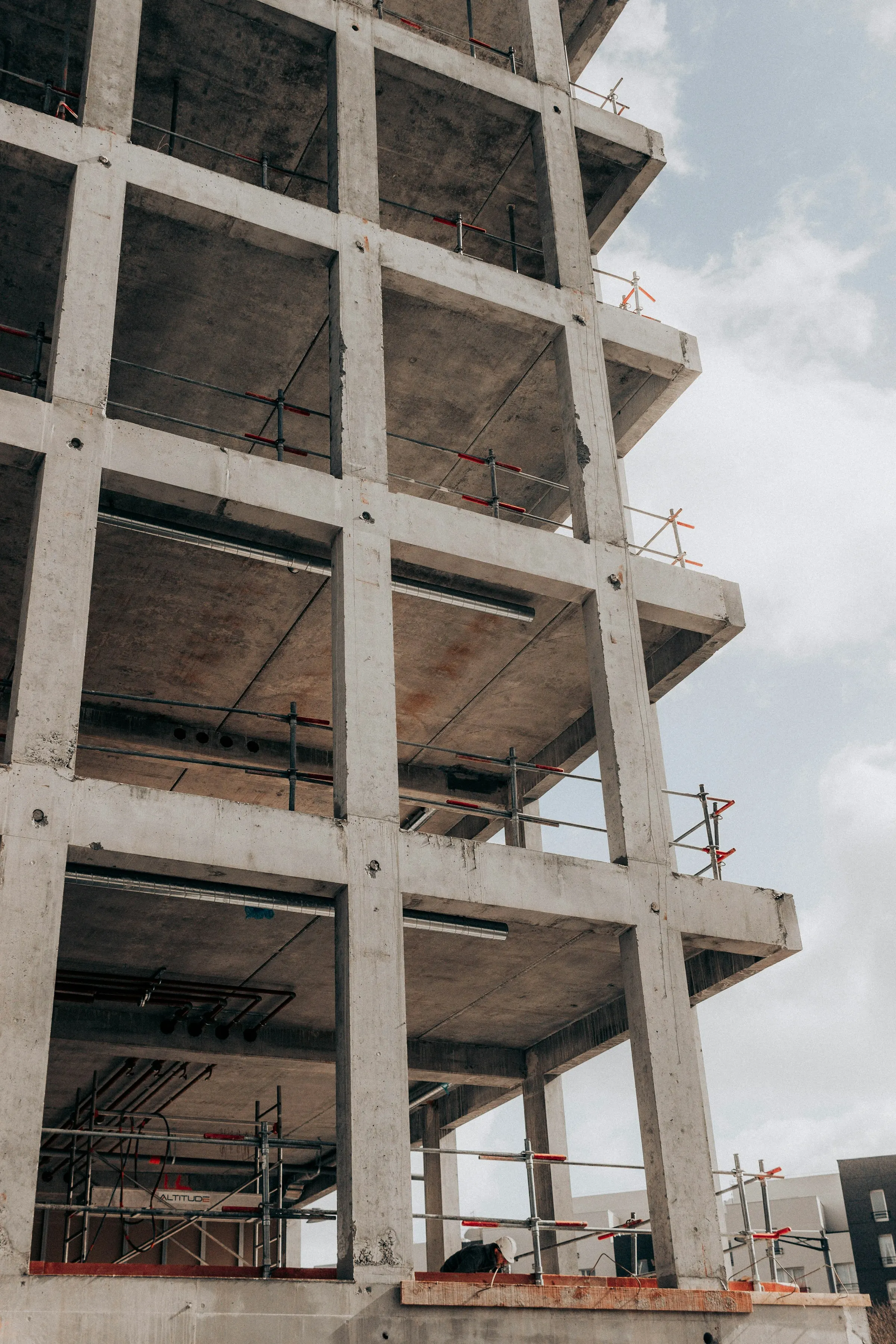 A concrete building frame under construction: columns and floor slabs against the sky, with edge protection along the slabs.